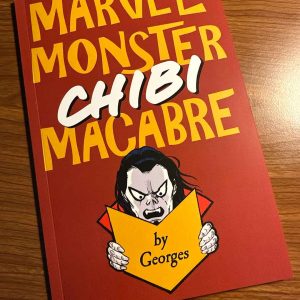 Red sketchbook cover titled “Marvel Monster Chibi Macabre” in bold yellow and white lettering on a red background. A chibi-style vampire with pale skin, black hair, and fangs peers over a yellow book shape reading “by Georges,” set on a wooden surface.